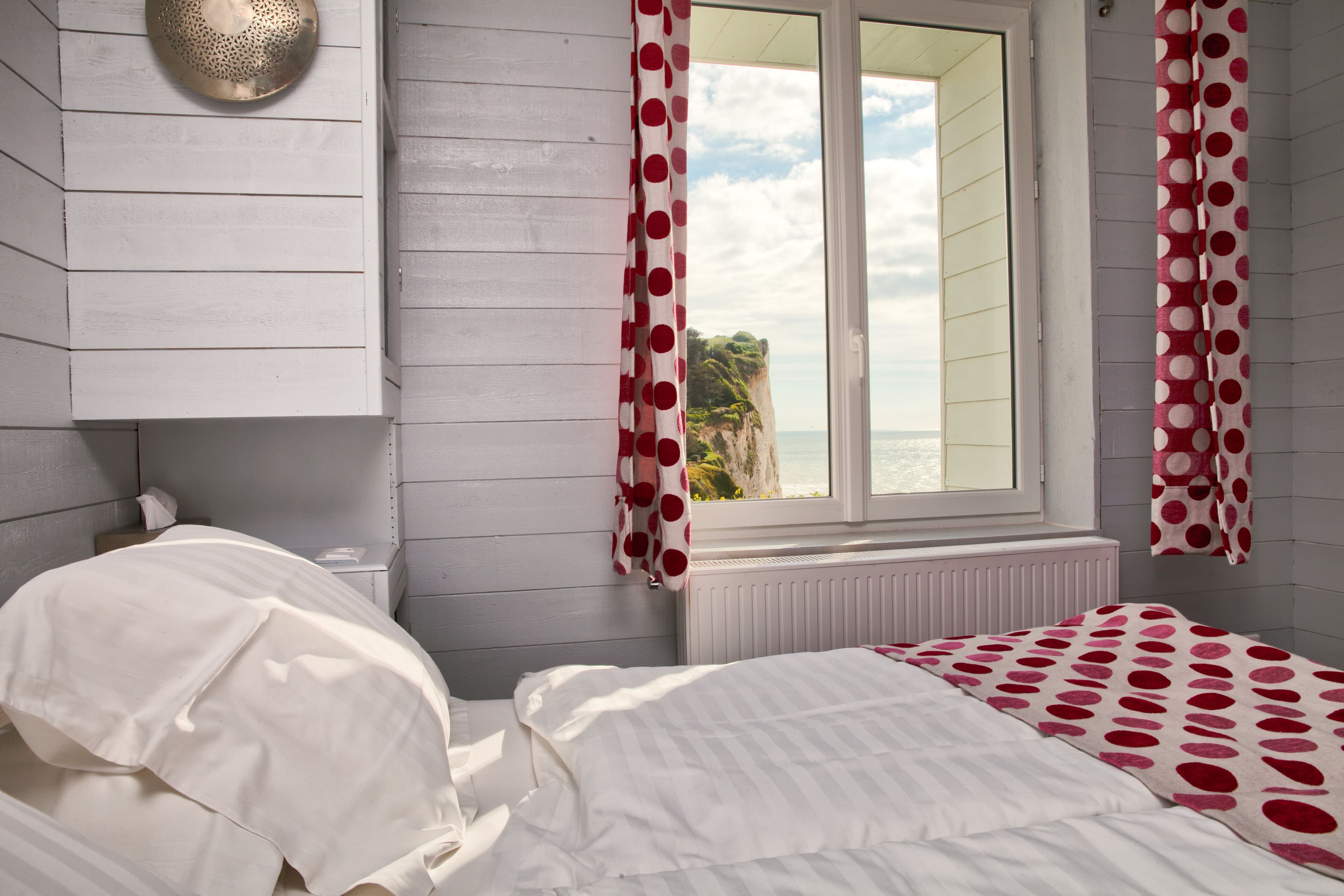 A bedroom with a bed, a window with curtains, a radiator, and a wall-mounted light fixture.