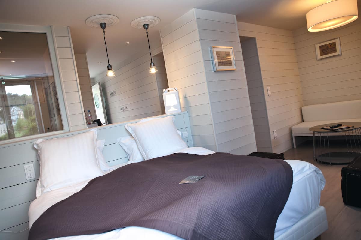 Un dormitorio moderno con una cama grande, mesitas de noche, un pequeño sofá y un rincón de comedor.