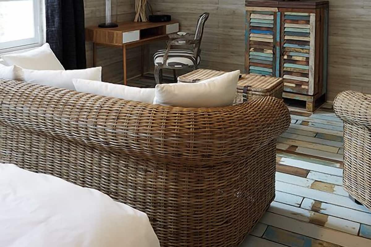 Un dormitorio con una cama grande, un sofá de mimbre, un armario de madera, un escritorio y un televisor montado en la pared.