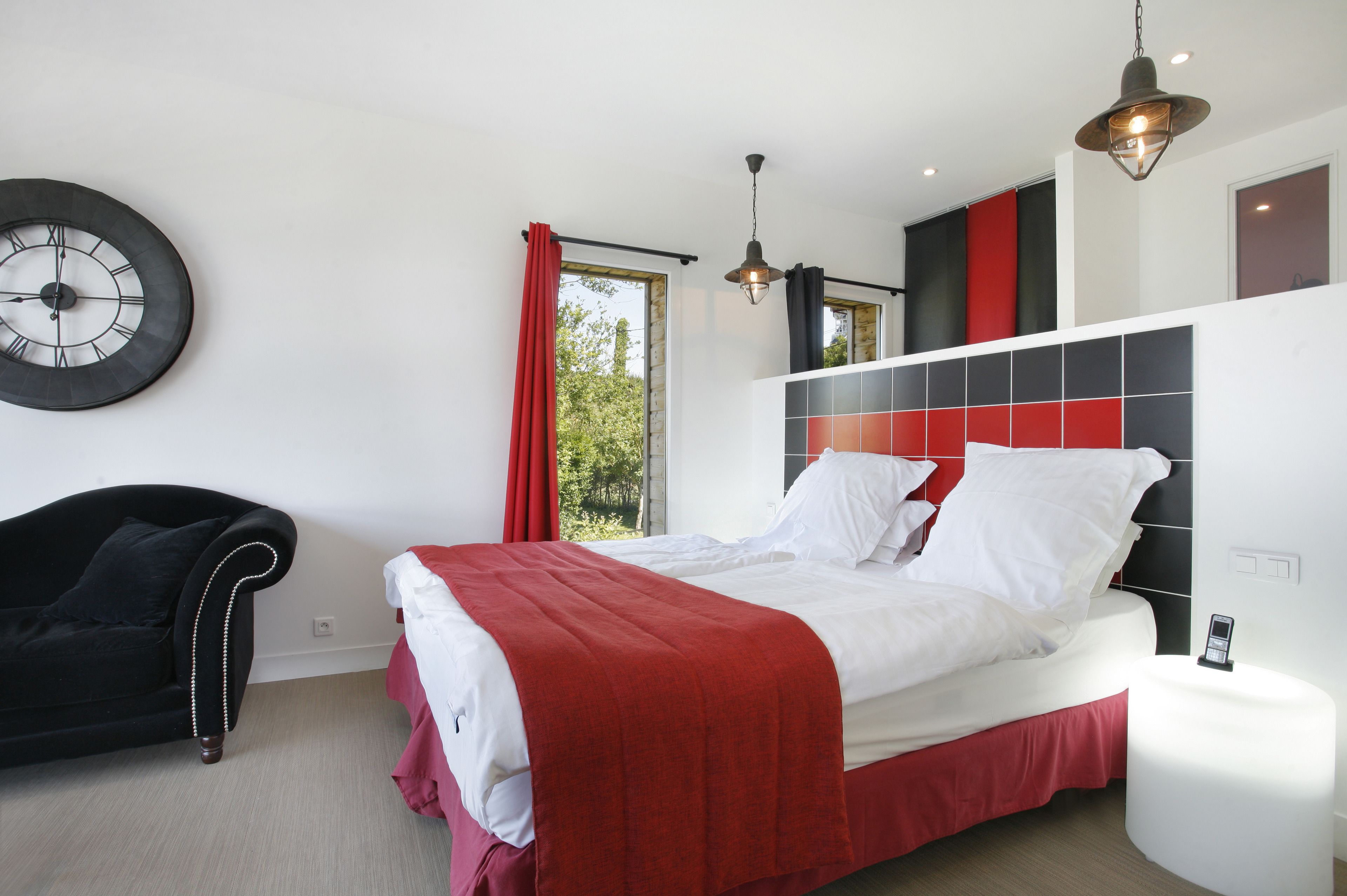 A modern bedroom with a large bed, a black armchair, a red and white color scheme, and a large wall clock.