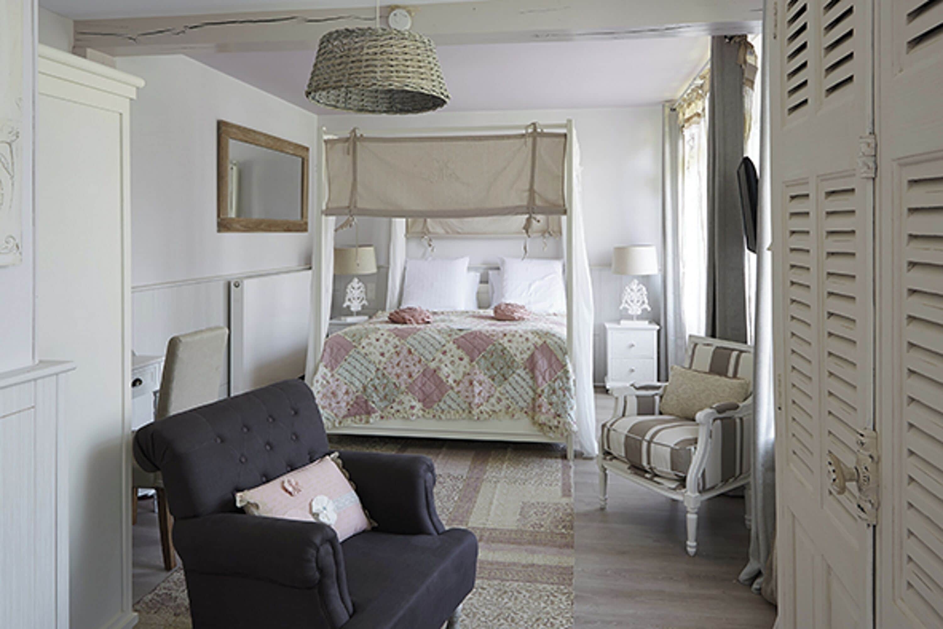 A bedroom with a four-poster bed, a chair, a nightstand, and a bedside table.