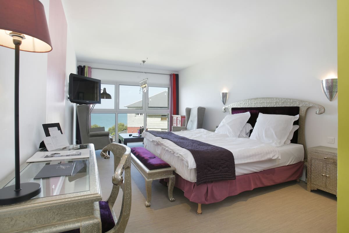 Habitación de hotel con cama, mesita de noche, lámpara, televisor y ventana con cortinas.