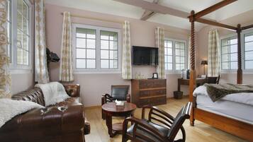 A bedroom with a four-poster bed, a wooden dresser, a television, and a seating area with a sofa and chairs.