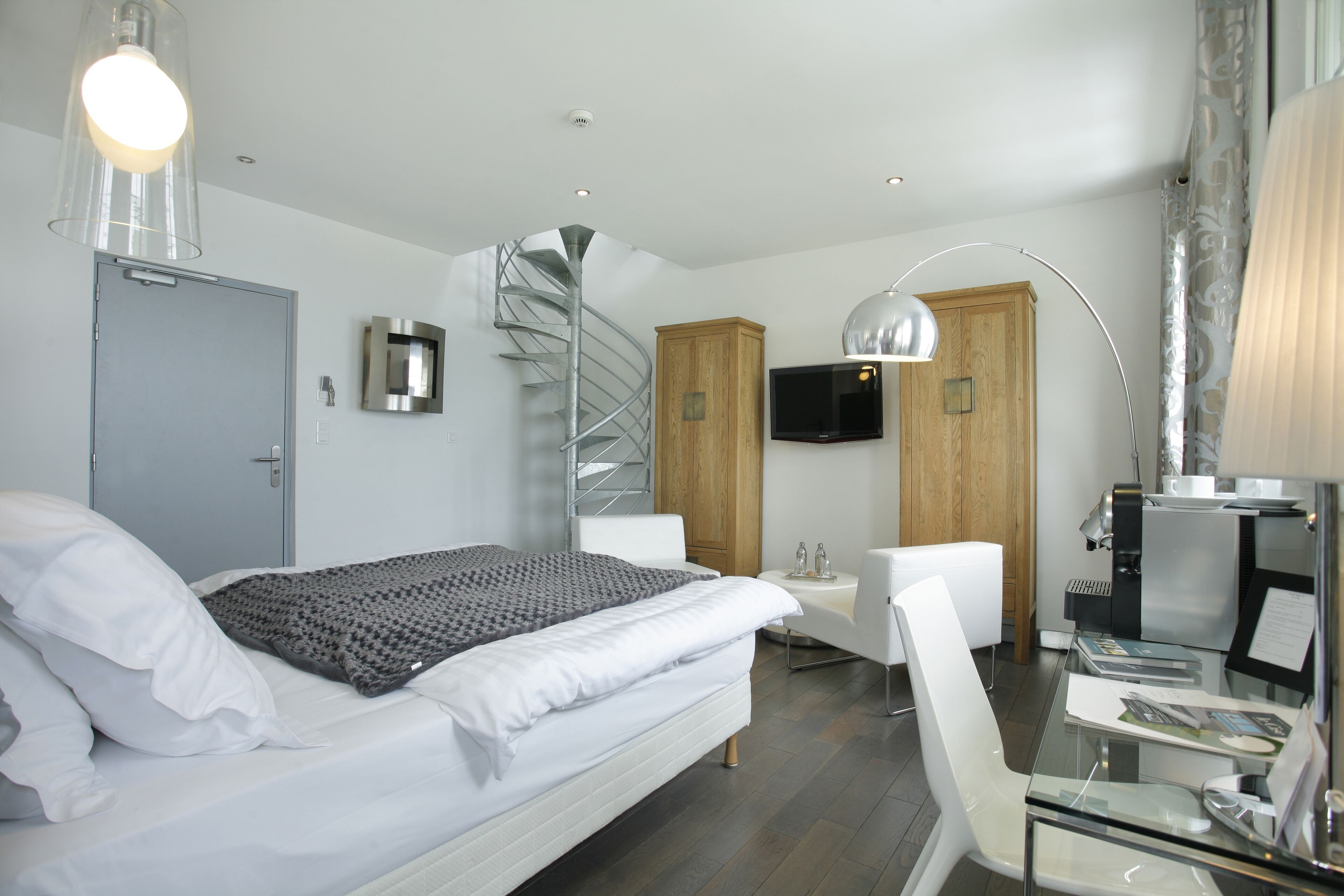 Una habitación de hotel moderna con cama, escritorio, silla, televisor y una escalera de caracol.
