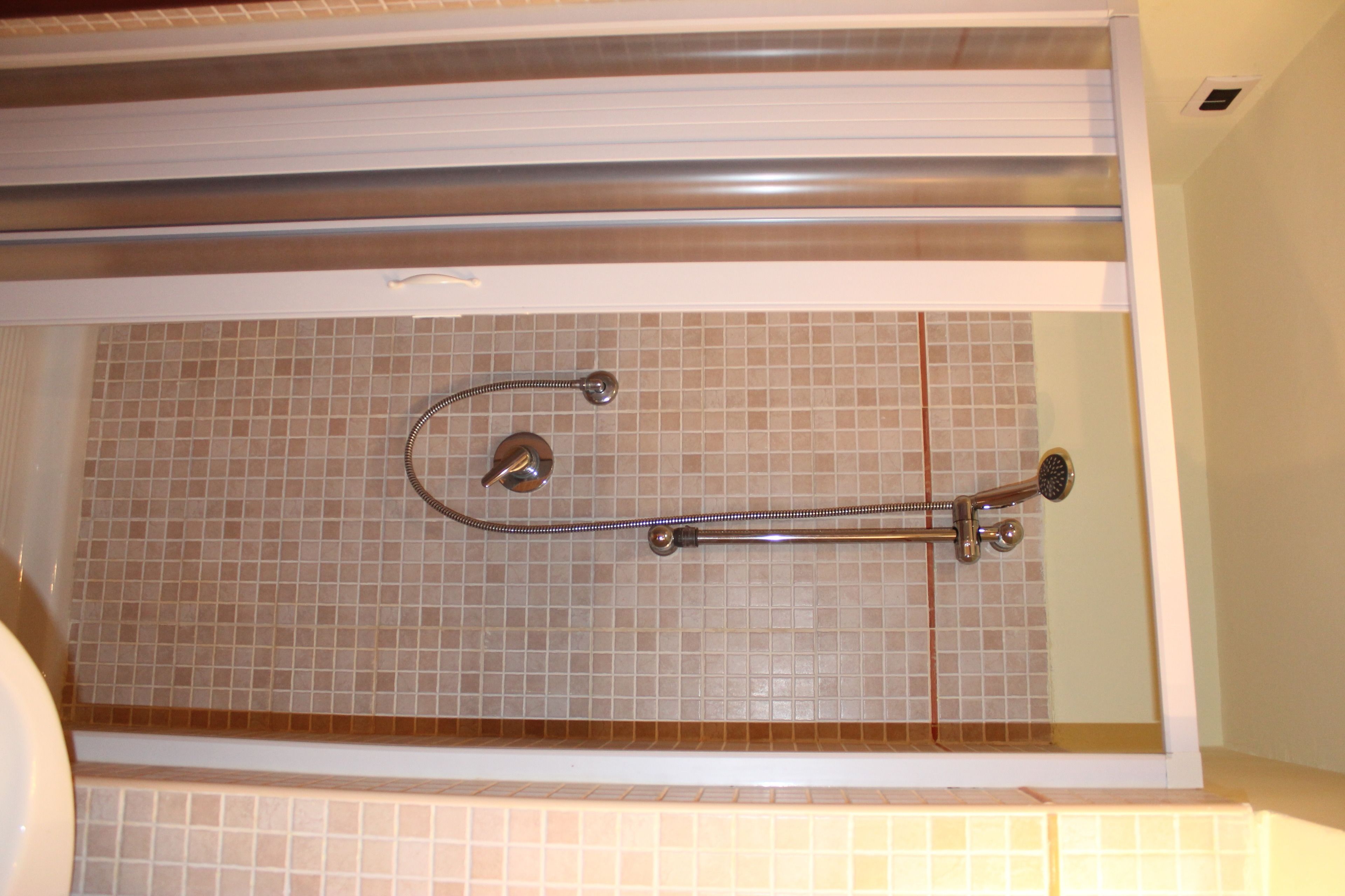 A shower with a grab bar, tiled walls, and a white bathtub.