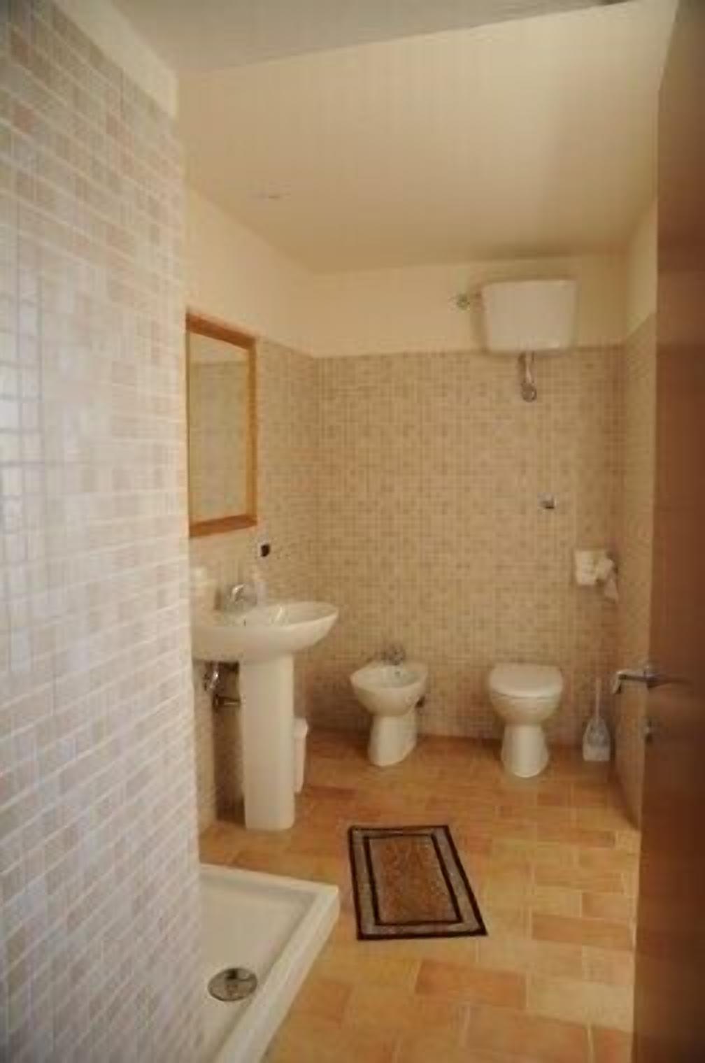 A bathroom with a sink, two toilets, a bidet, and a shower.