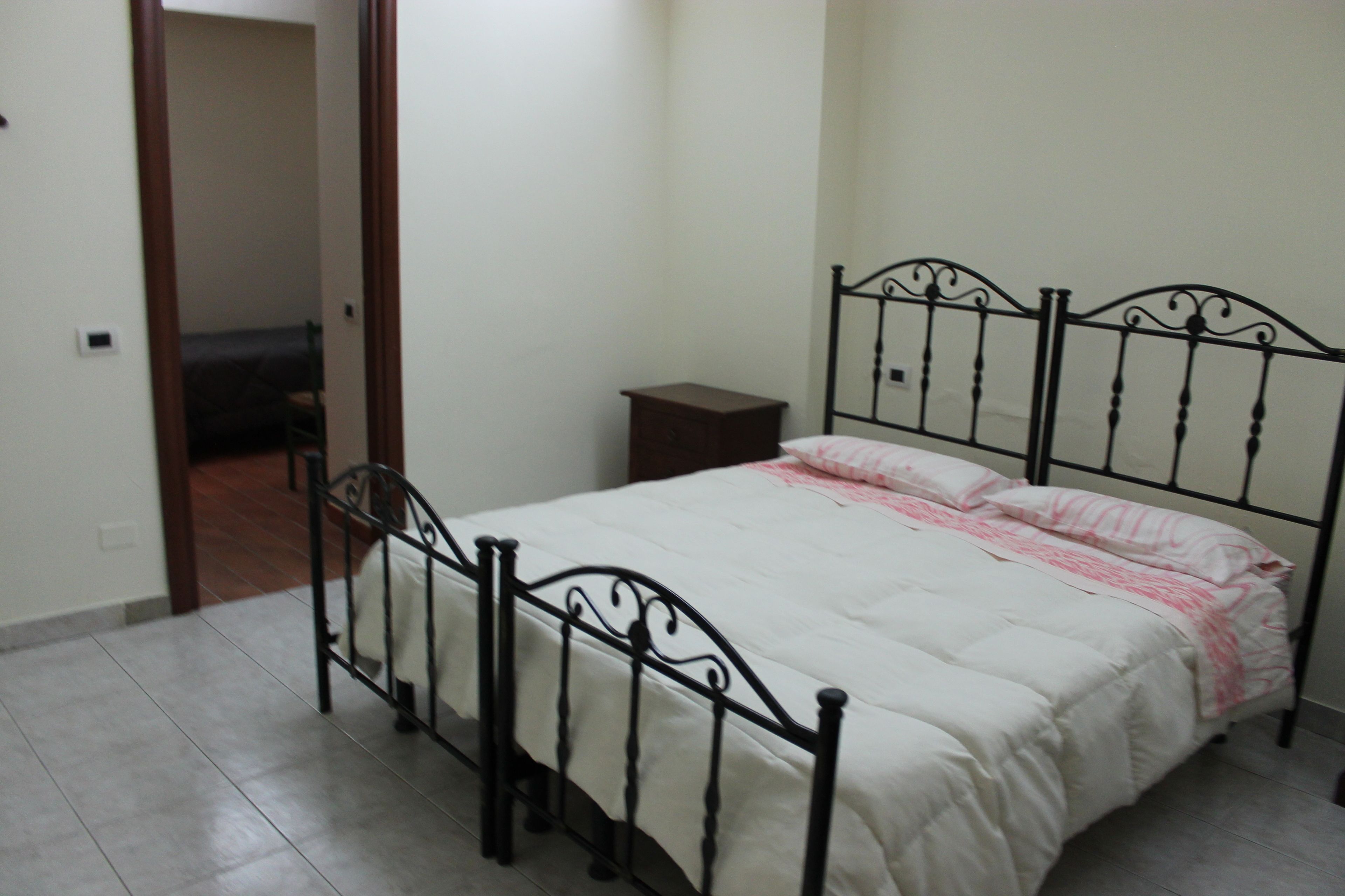 A bedroom with a bed, a nightstand, and a door leading to another room.
