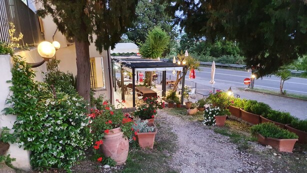 Un jardín con plantas en macetas, un sendero de grava y mobiliario exterior bajo una pérgola.