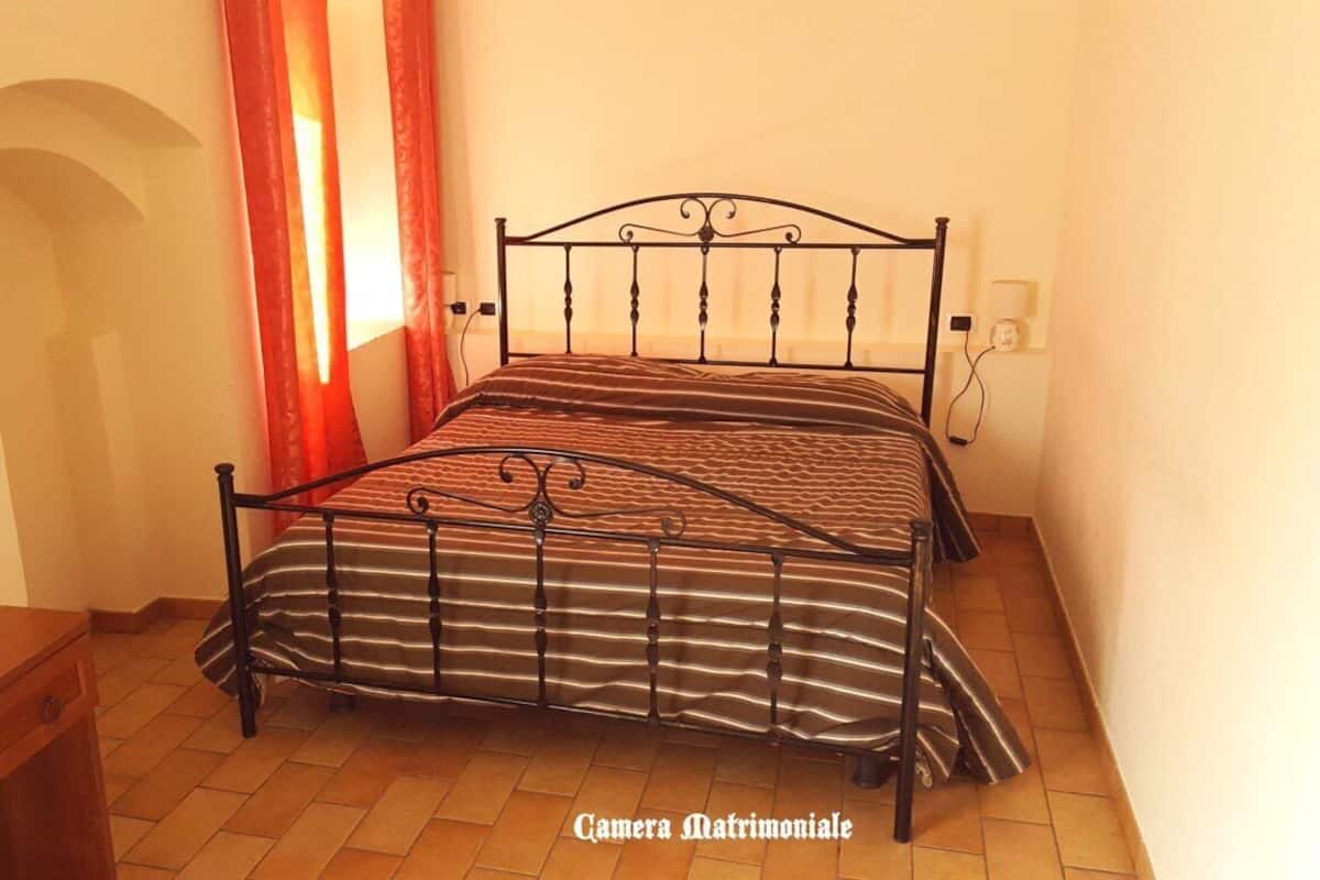 A single bed with a metal frame in a room with tiled flooring and a wooden nightstand.
