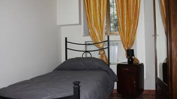 A single bed with a metal frame, a bedside table with a lamp, and a window with yellow curtains.
