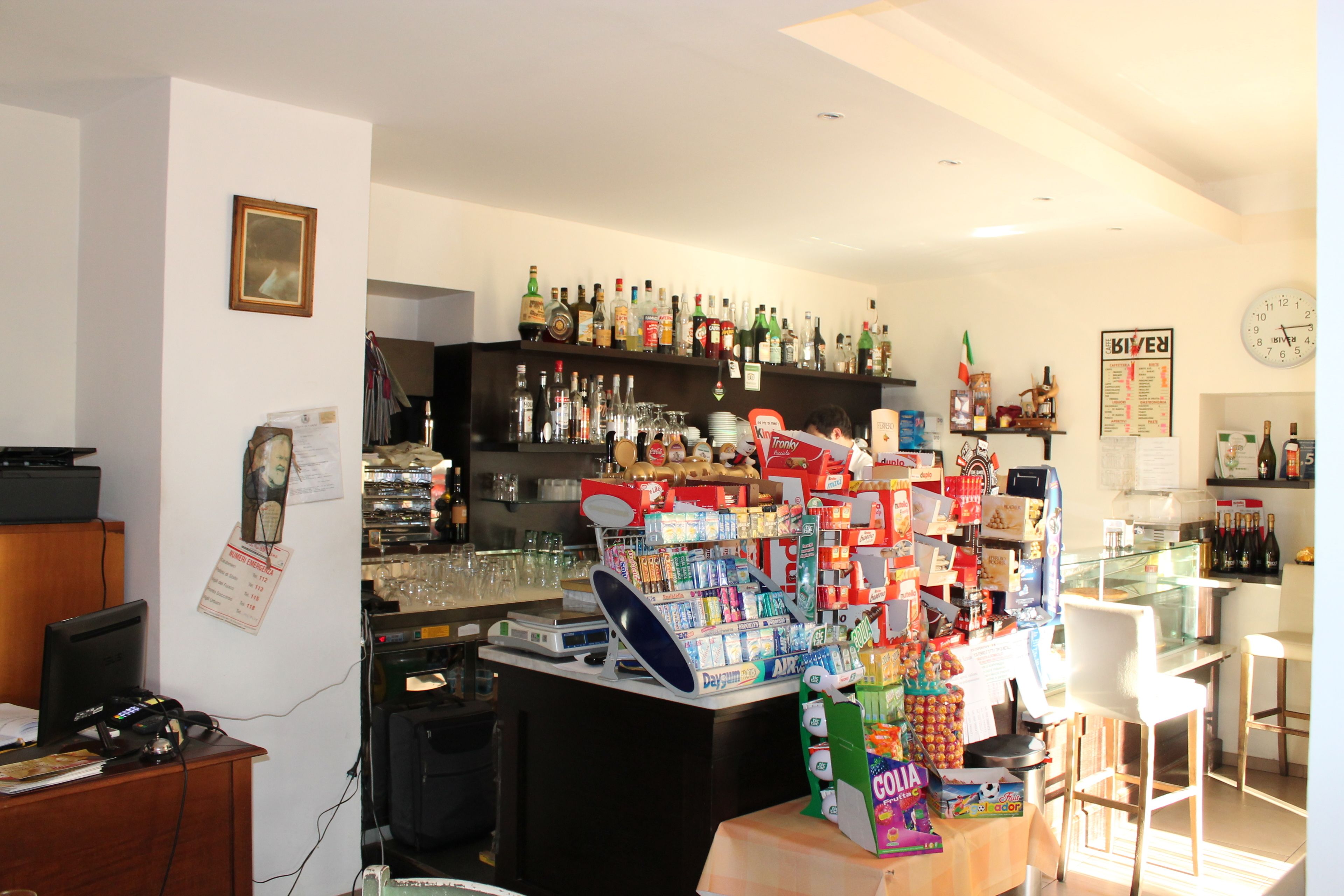 A bar area with shelves of alcohol, a cash register, and a counter with snacks and drinks.