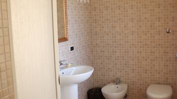 Une salle de bain équipée d’un lavabo, d’un bidet, de toilettes et de murs carrelés.