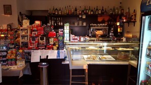 Una panadería con un escaparate de pasteles, estantes de bebidas embotelladas y diversos productos envasados.