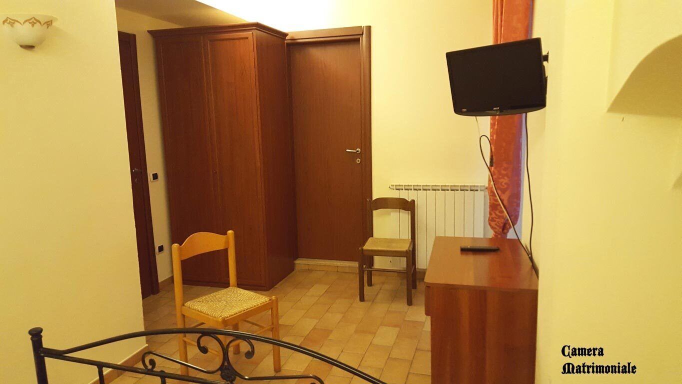 Una habitación con puerta de madera, una silla, una mesita y televisor montado en la pared.