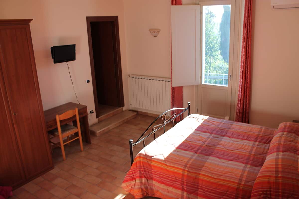 A bedroom with a bed, a desk, a chair, a wardrobe, a radiator, and a window with curtains.