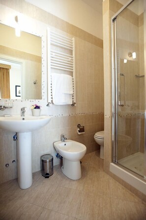 Baño con lavamanos, bidé, inodoro y ducha con mampara de vidrio.