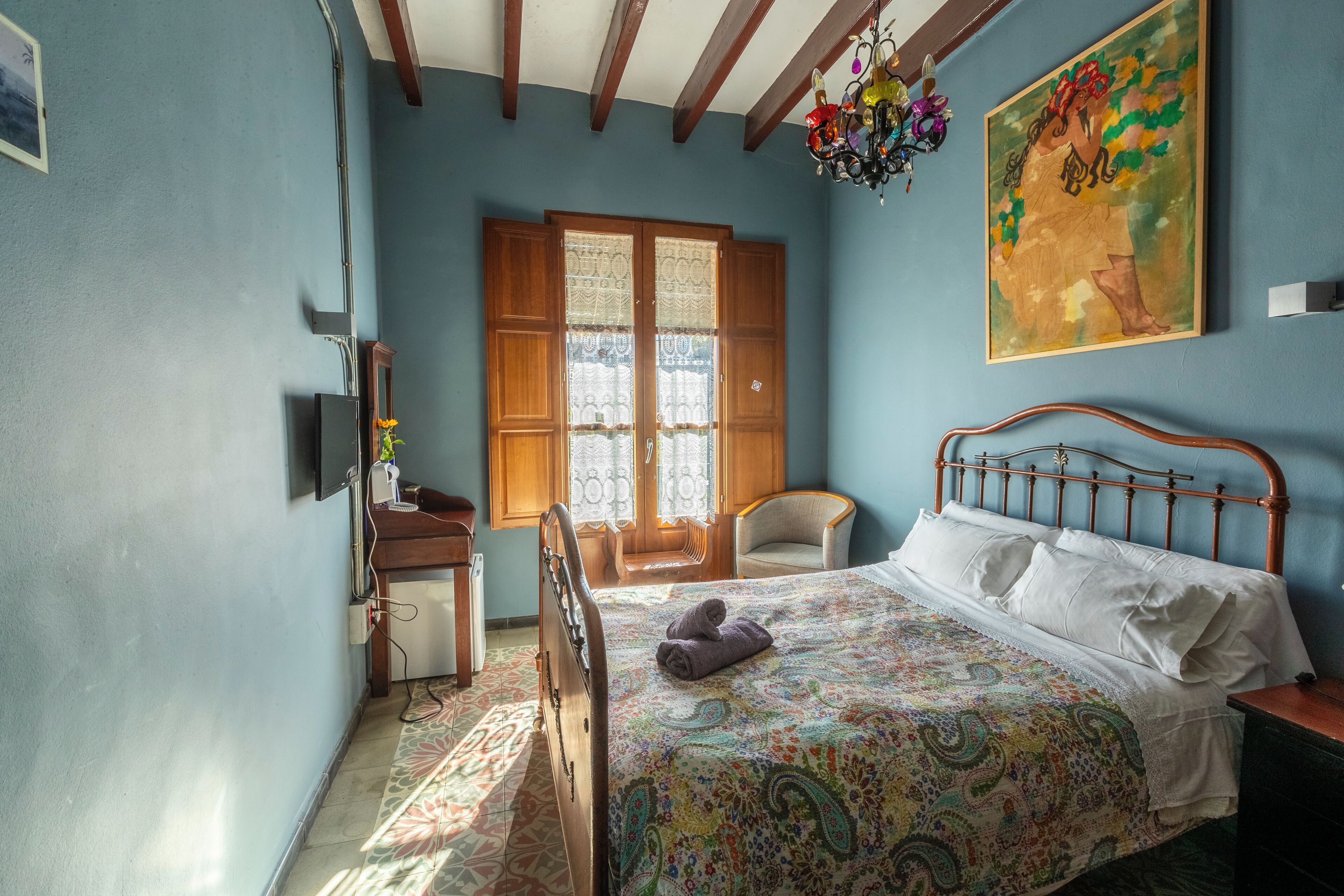 Un dormitorio con cama, una silla, un escritorio y una ventana con cortinas.