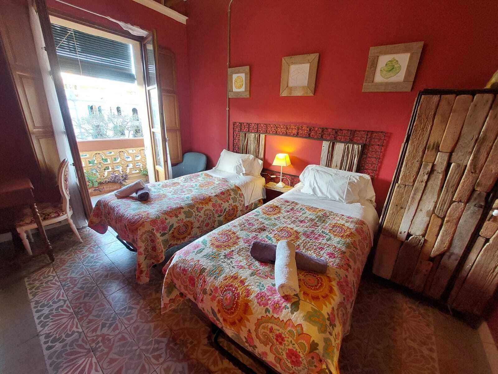 A room with two beds, a wooden wardrobe, a chair, and a window with a view.