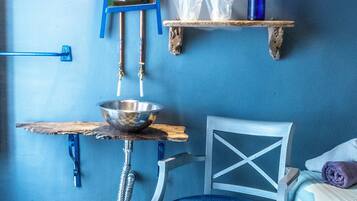 Un baño con pared azul, un lavabo con espejo, un perchero, una silla azul y un estante pequeño con un jarrón.