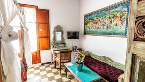 A room with a checkered floor, a wooden door, a television, a painting, a sofa, and a table with a vase of flowers. - Ibiza Boutique Guest House (Ibiza Town)