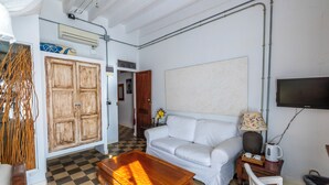A living room with a checkered floor, a white sofa, a wooden coffee table, and a television mounted on the wall. - Ibiza Boutique Guest House (Ibiza Town)
