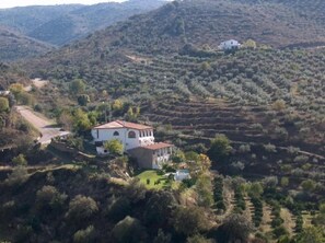 Une villa blanche avec un toit rouge, entourée de champs en terrasses et de collines.