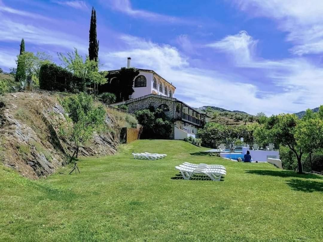 A villa with a stone staircase leading to a white building, a pool, and a grassy area with lounge chairs.