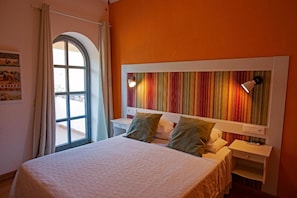 A hotel room with a bed, a nightstand, a window with curtains, and a colorful striped headboard.