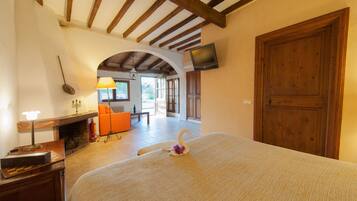 Una camera d'albergo con un letto, un caminetto, una televisione a parete e una porta ad arco che conduce a un'altra stanza.