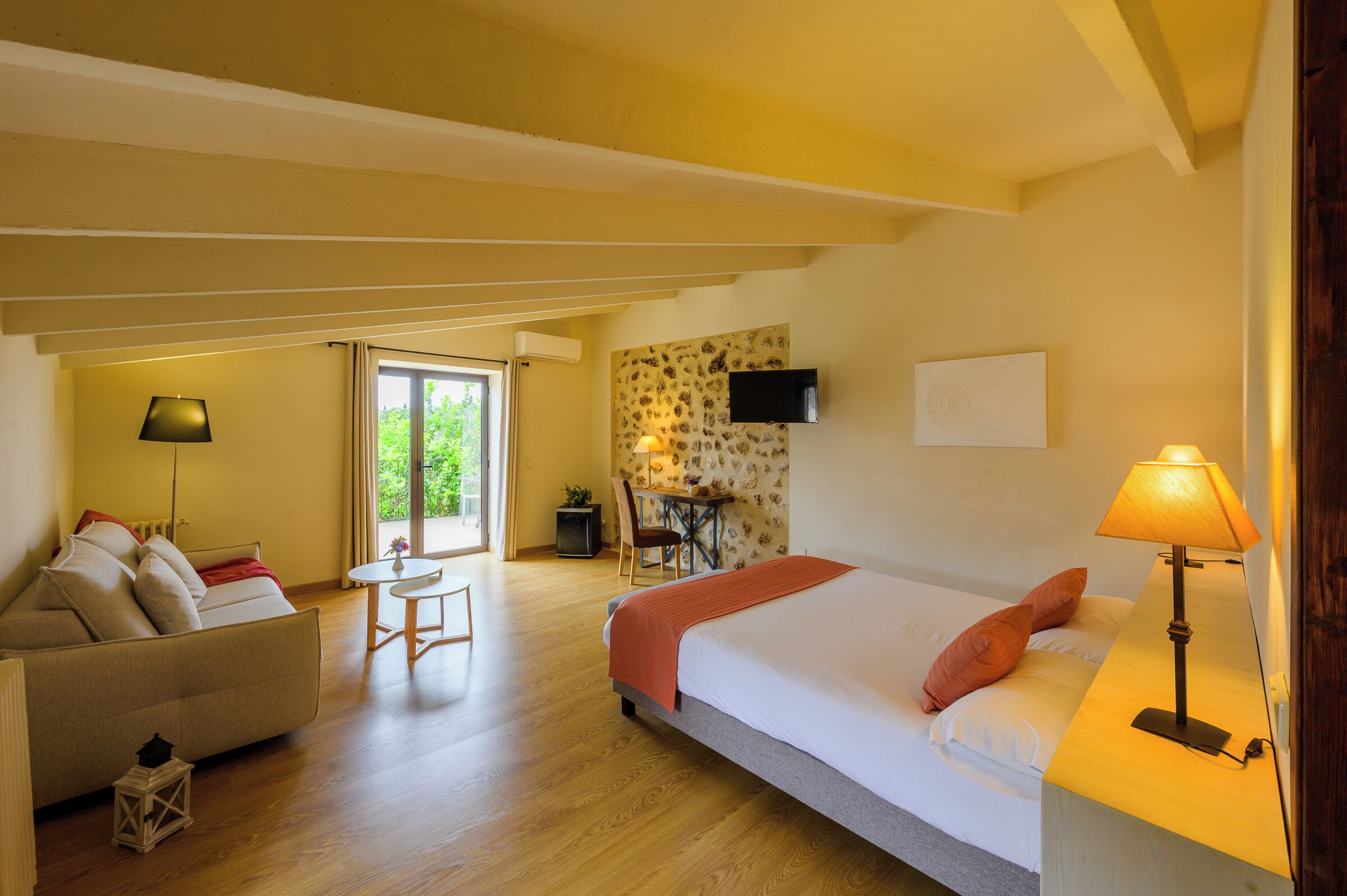A hotel room with a bed, a sofa, a desk with a chair, and a TV mounted on the wall.
