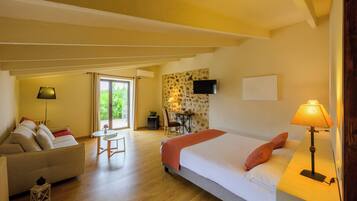 A hotel room with a bed, a sofa, a desk with a chair, and a TV mounted on the wall.