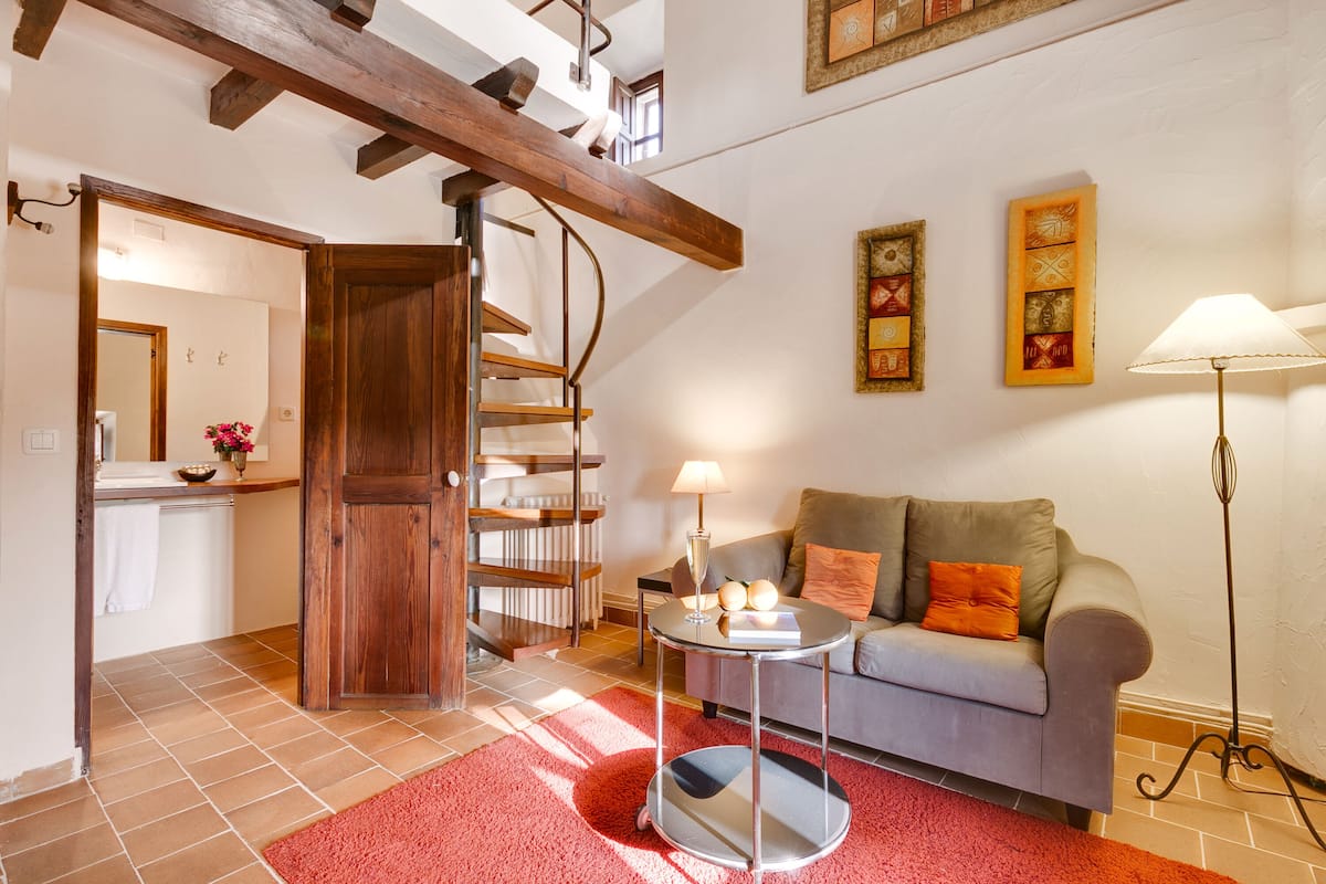 A living room with a grey sofa, a red rug, a wooden staircase, and a floor lamp.