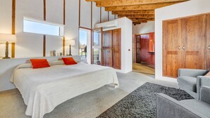 Een slaapkamer met een groot bed, een grijze bank, een houten garderobe en een raam.