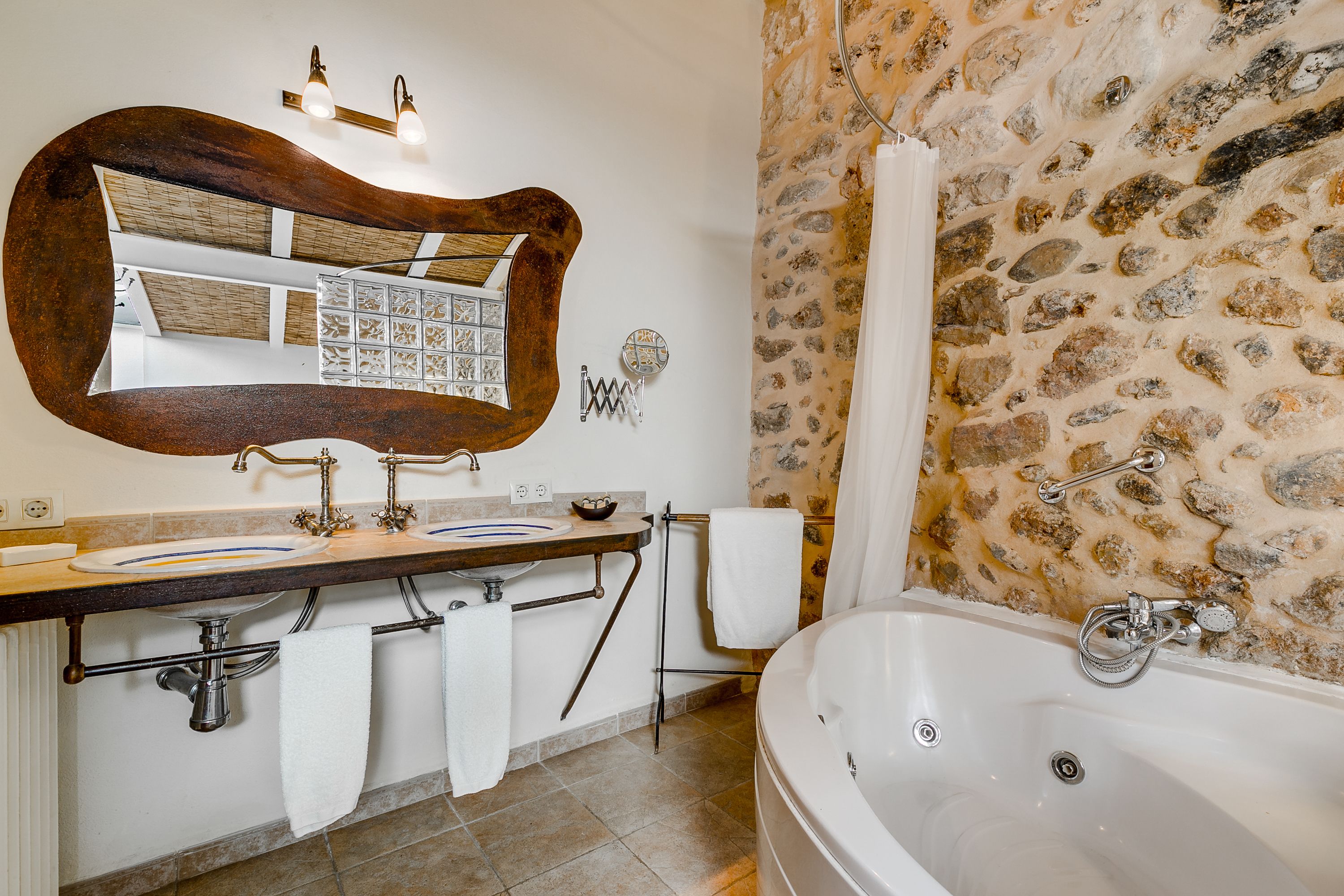 Un baño con pared de piedra, un espejo grande, dos lavamanos, una bañera y un perchero para toallas.