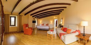 A spacious room with wooden floors, a bed, a sofa, a chair, and a small table with a lamp. - Agroturismo Son Pons (Sa Pobla)