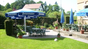 An outdoor seating area with tables and chairs under a blue umbrella with 'Peterstaler' branding. - Gasthaus Finken (Oppenau)
