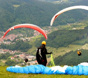 A person preparing to rappel down a hill with a parachute, overlooking a village with houses and greenery.