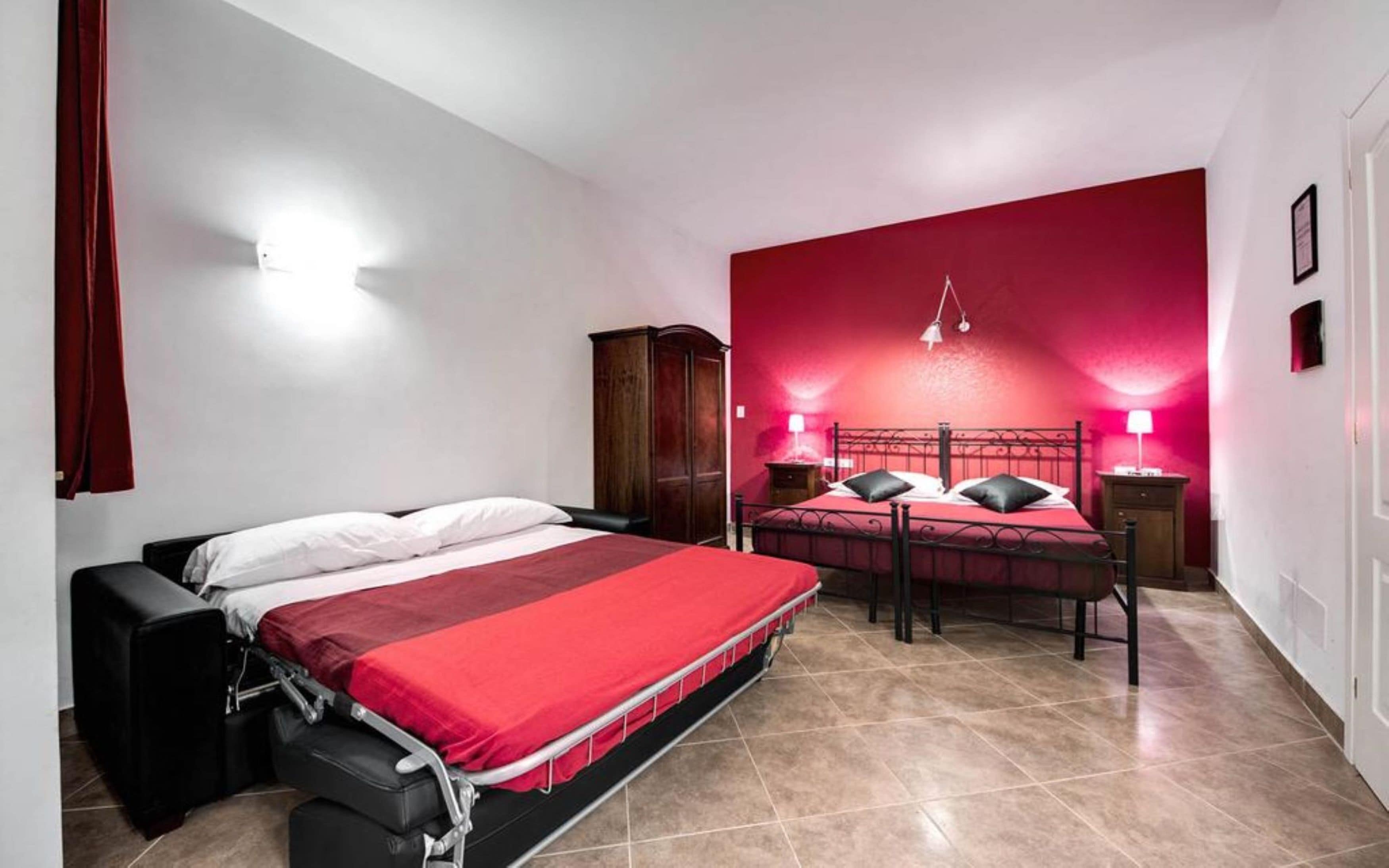 A bedroom with two beds, a wardrobe, and a red accent wall.
