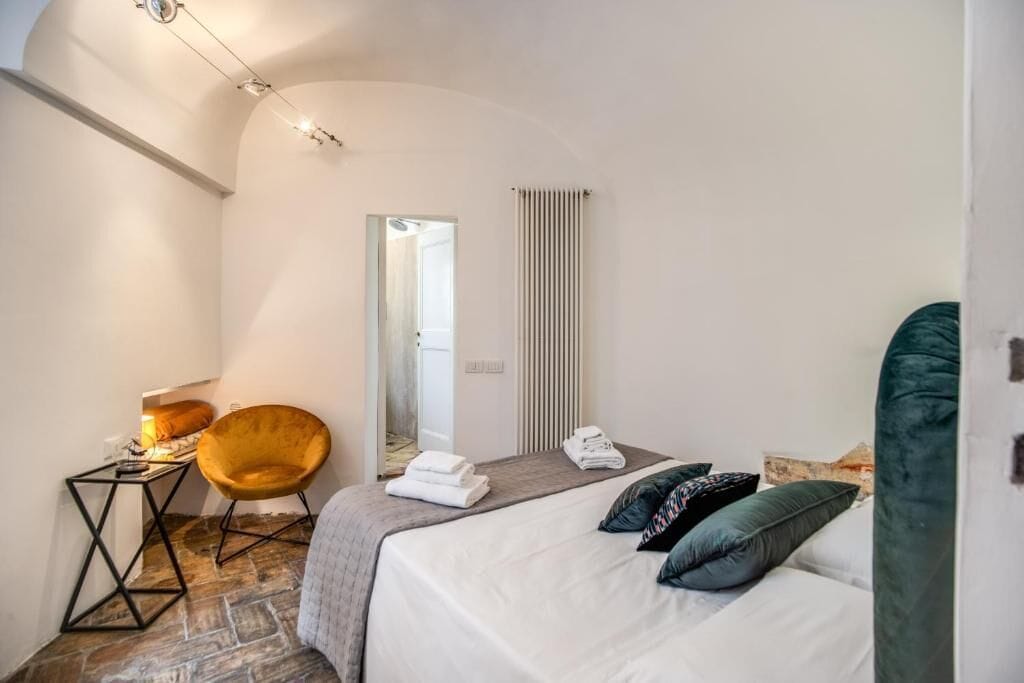 Ein Schlafzimmer mit einem Bett, einem Sessel, einem kleinen Tisch, einem Heizkörper und einem Spiegel.