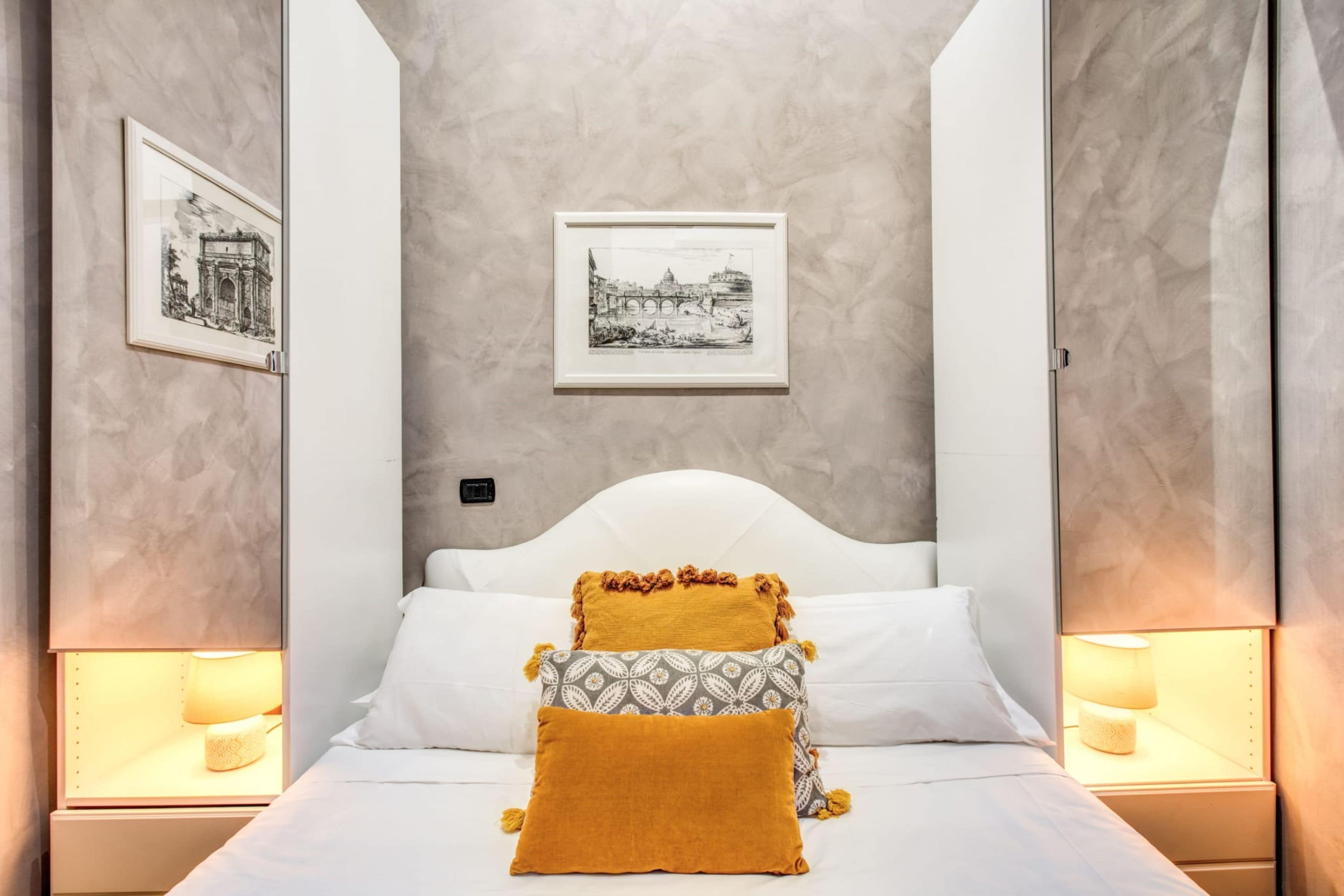 A neatly arranged bedroom with a white bed, two pillows, two bedside lamps, and two framed pictures on the wall.