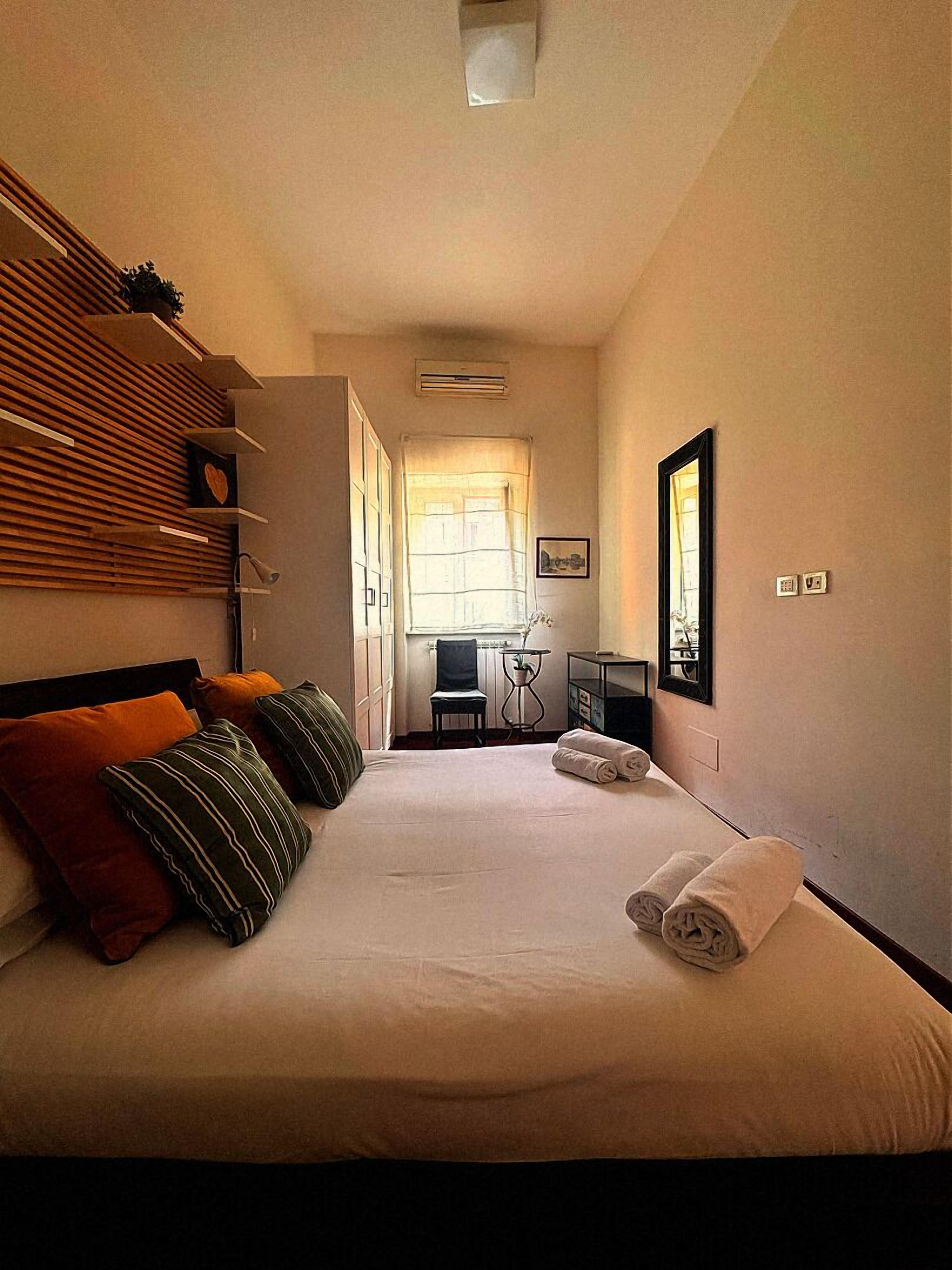 A hotel room with a bed, pillows, a desk, a chair, a TV, and a window.