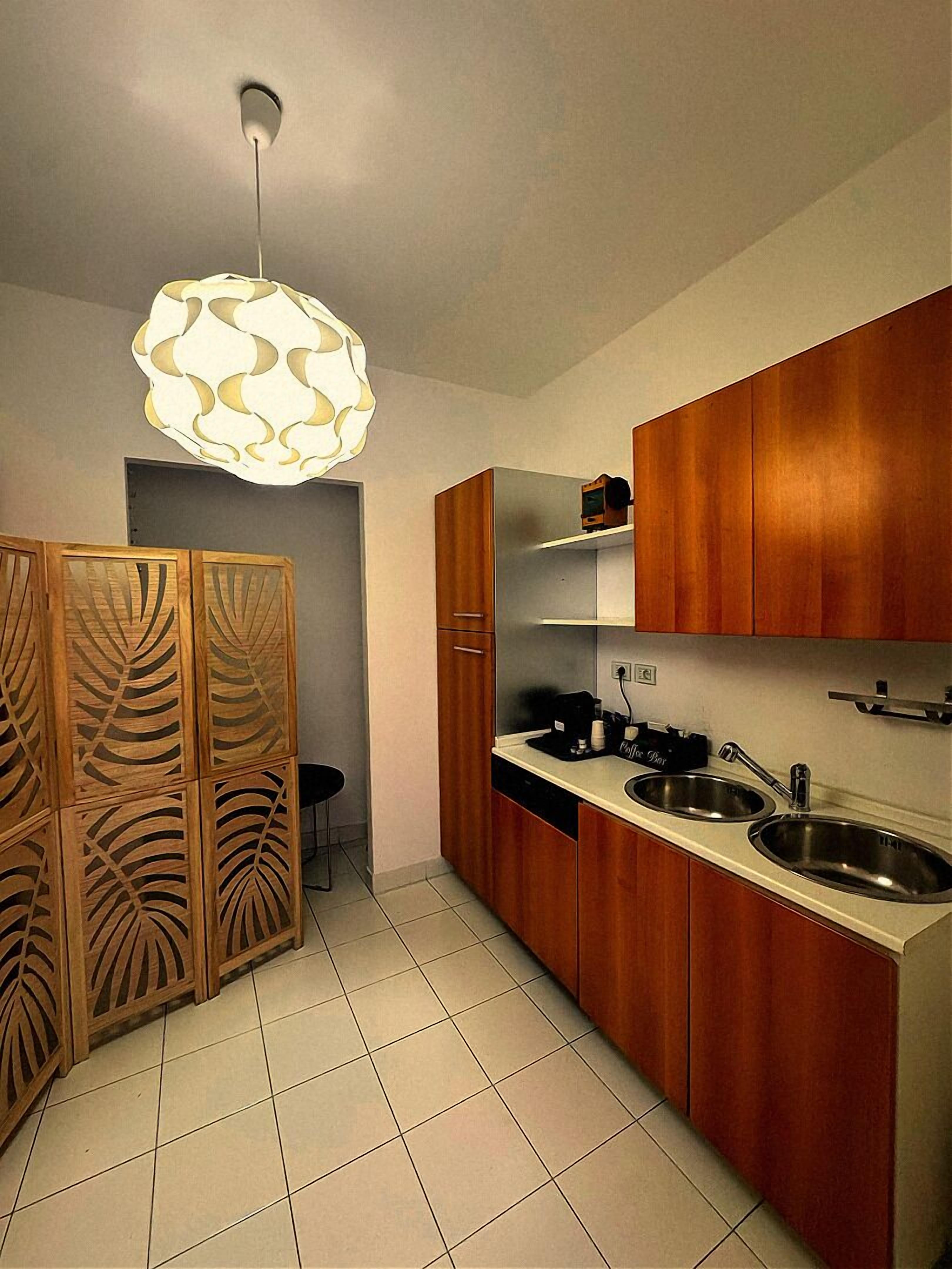 A kitchen with wooden cabinets, a sink, a coffee machine, and a pendant light.