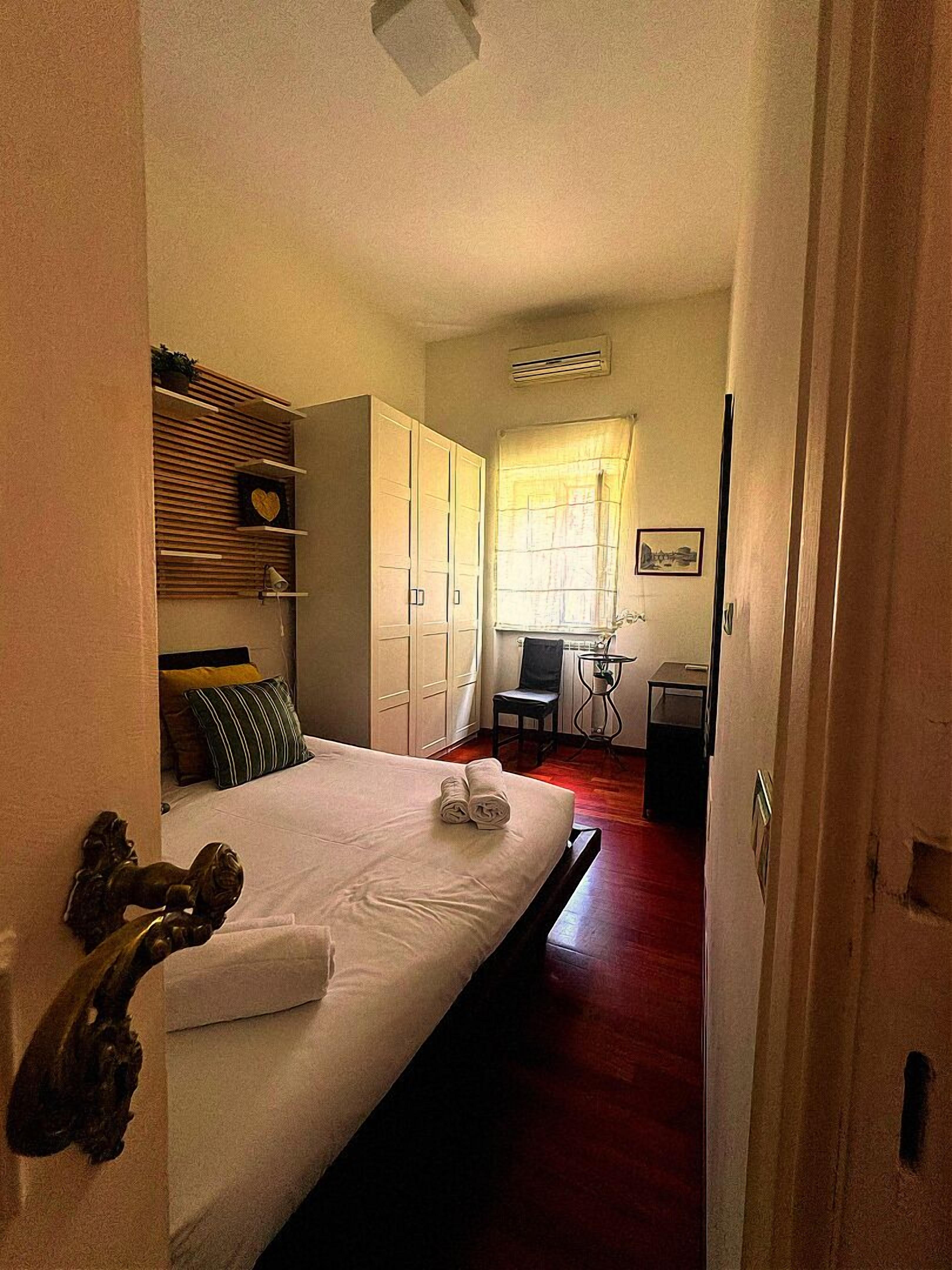 A hotel room with a bed, a desk, a chair, a wardrobe, and a window with curtains.