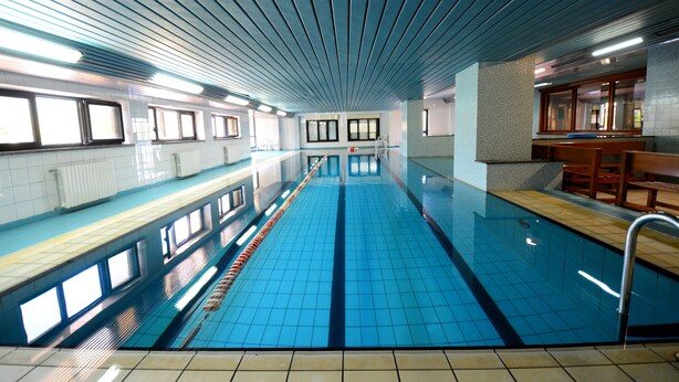 Ein langer, überdachter Schwimmteich mit gefliesten Wänden und einer Decke mit parallelen Linien.