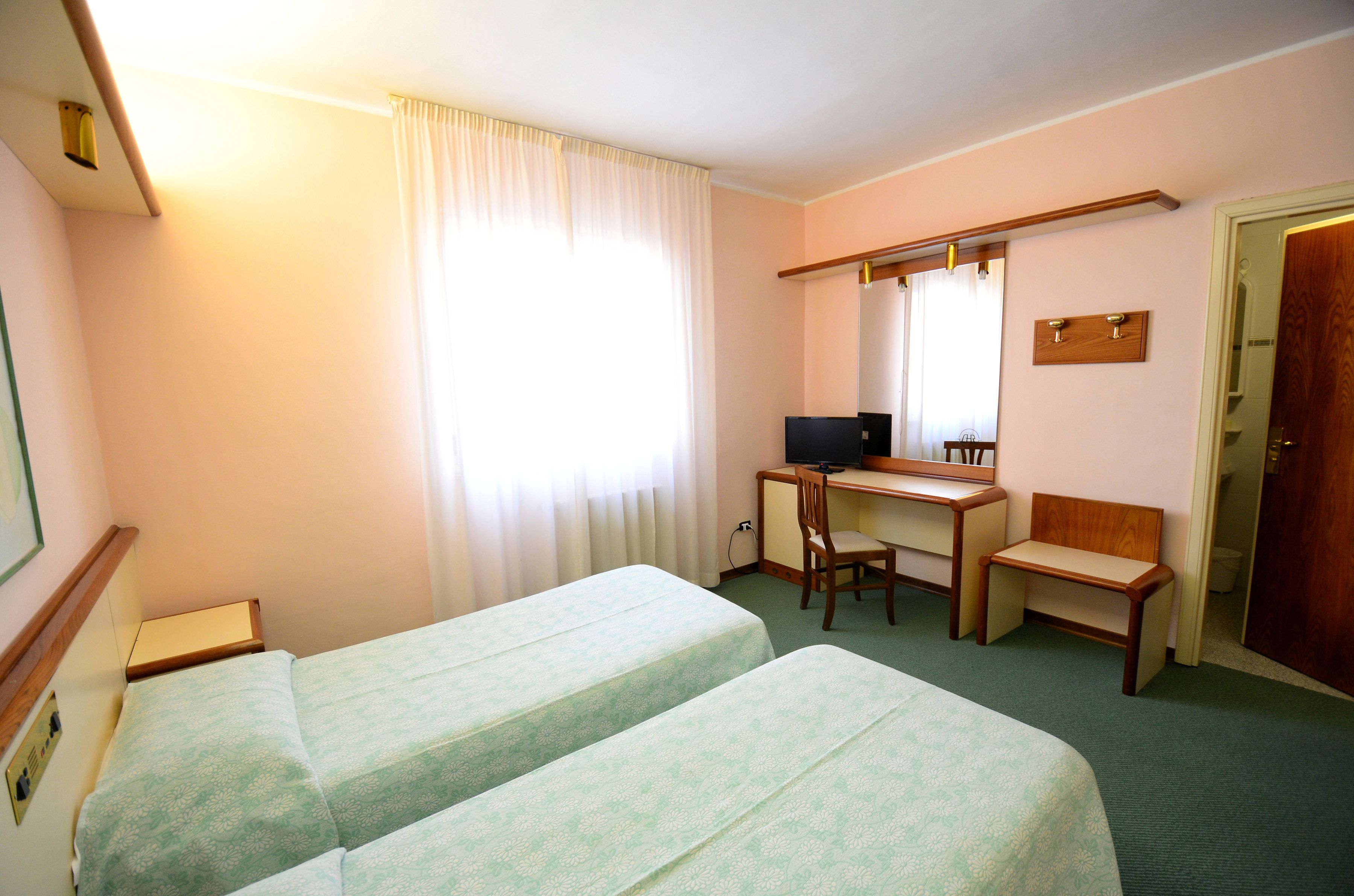 Una camera d'albergo con due letti, una scrivania, una sedia, una televisione e una porta.