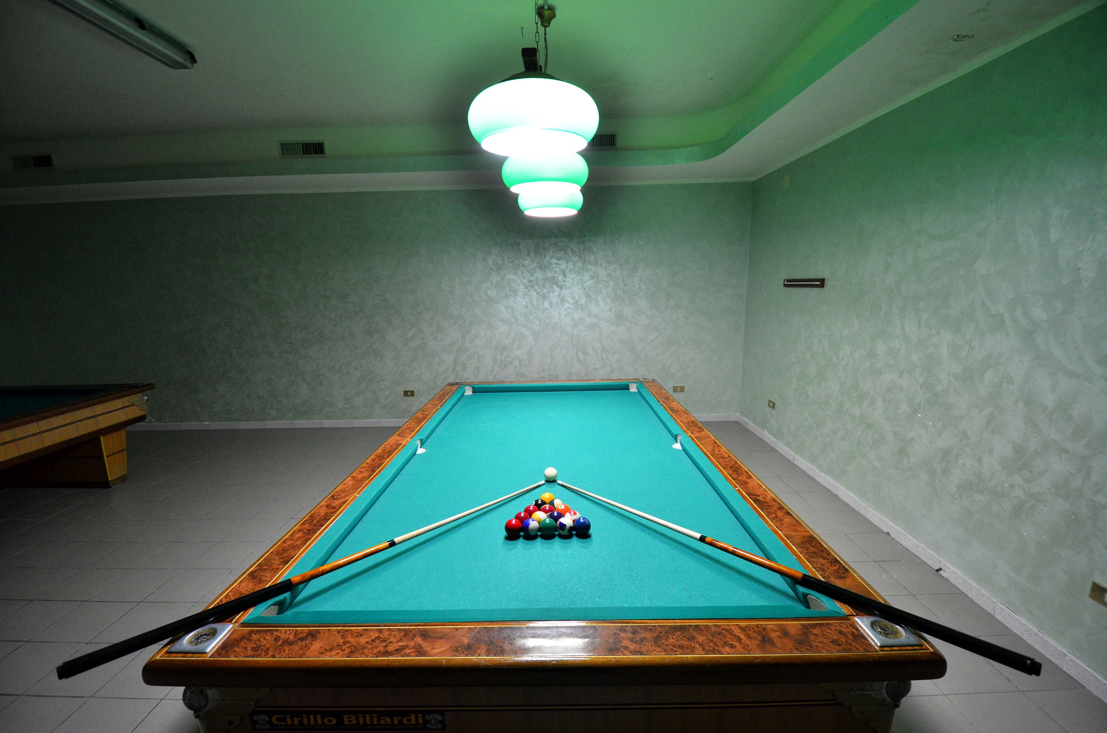 A pool table with balls and cues, a green wall, and a ceiling light fixture.