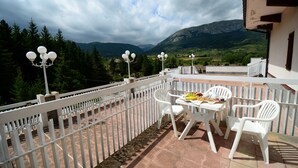 Ein Balkon mit weißen Stühlen und einem Tisch, mit Blick auf eine gebirgige Landschaft.