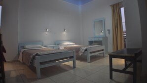 A bedroom with two beds, a small table, a nightstand, a mirror, and a ceiling light. - Zouboulia (Kos)