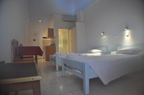 A bedroom with a bed, a desk, and a chair. There is a door leading to another room. - Zouboulia (Kos)