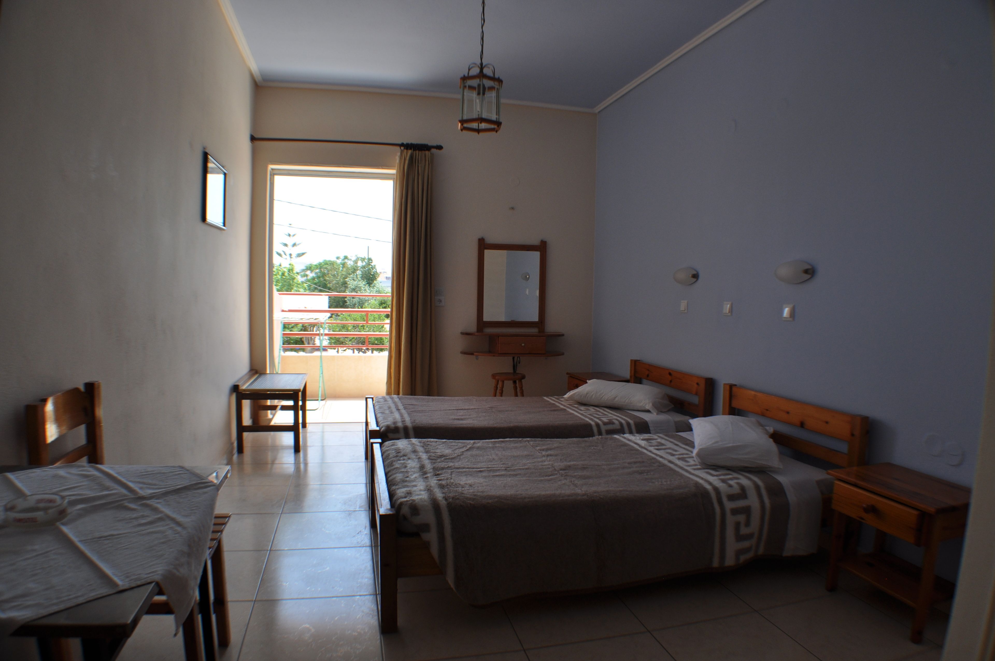 A hotel room with two beds, a dining table, a small table, and a balcony with a view.